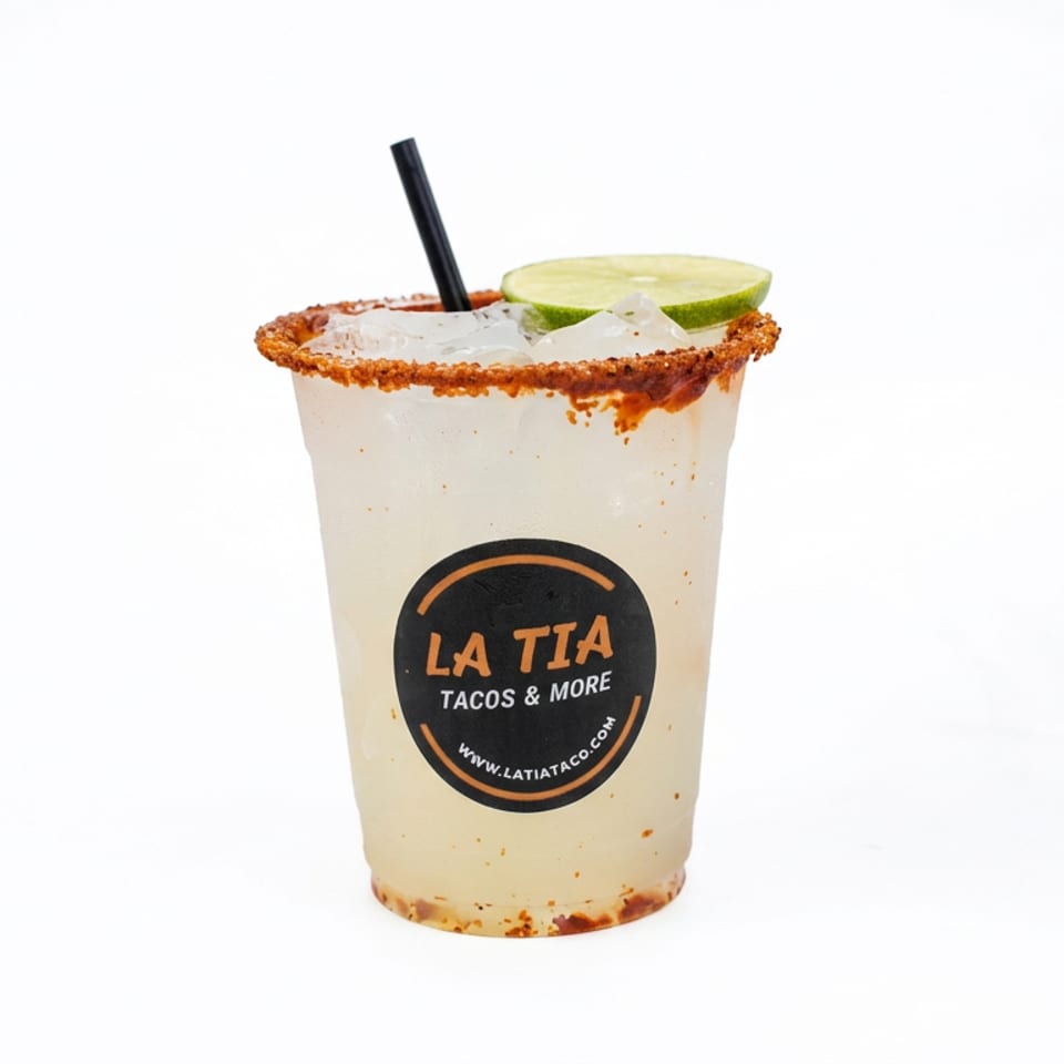 Chilled lime drink in a glass with a chili-salt rim, lime wedge, straw, and La Tia Tacos & More logo.